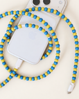 Blue and yellow USB-C beaded cable looped around an iPhone on cream background