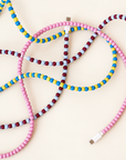Pink, blue and yellow, and burgundy and light blue USB-C beaded cables laid out on cream background