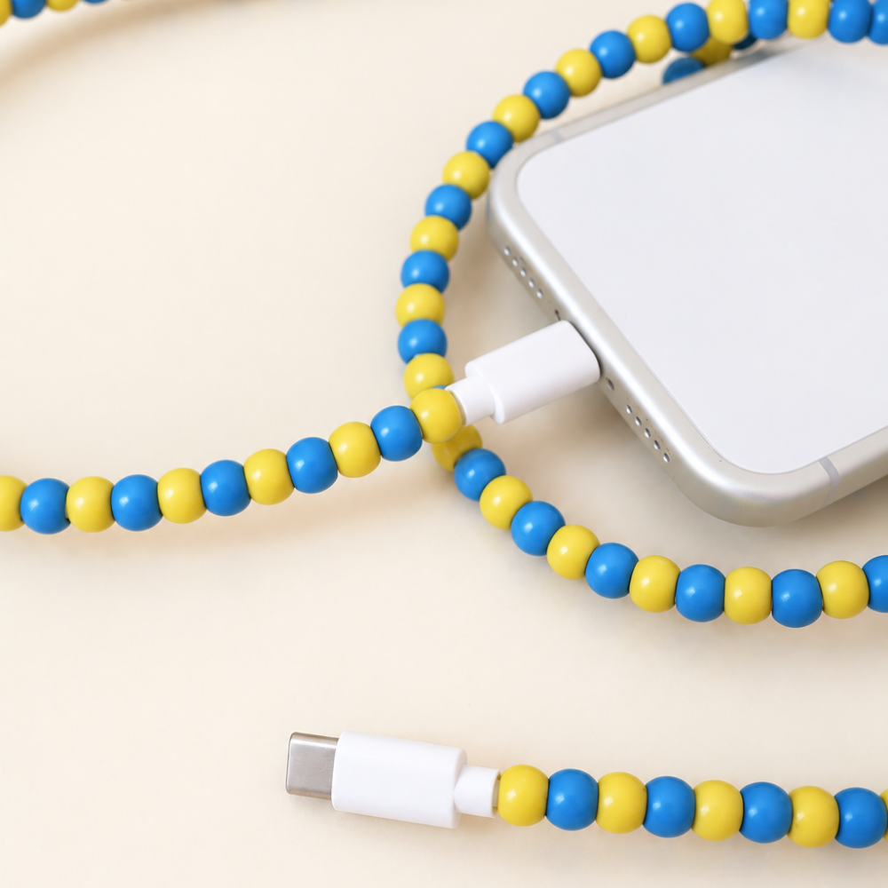 Blue and yellow USB-C beaded cable connected to an iPhone on cream background