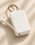 Ivory Posh Tech Keychain Power Bank with gold-tone key ring and built-in charging cable on beige linen